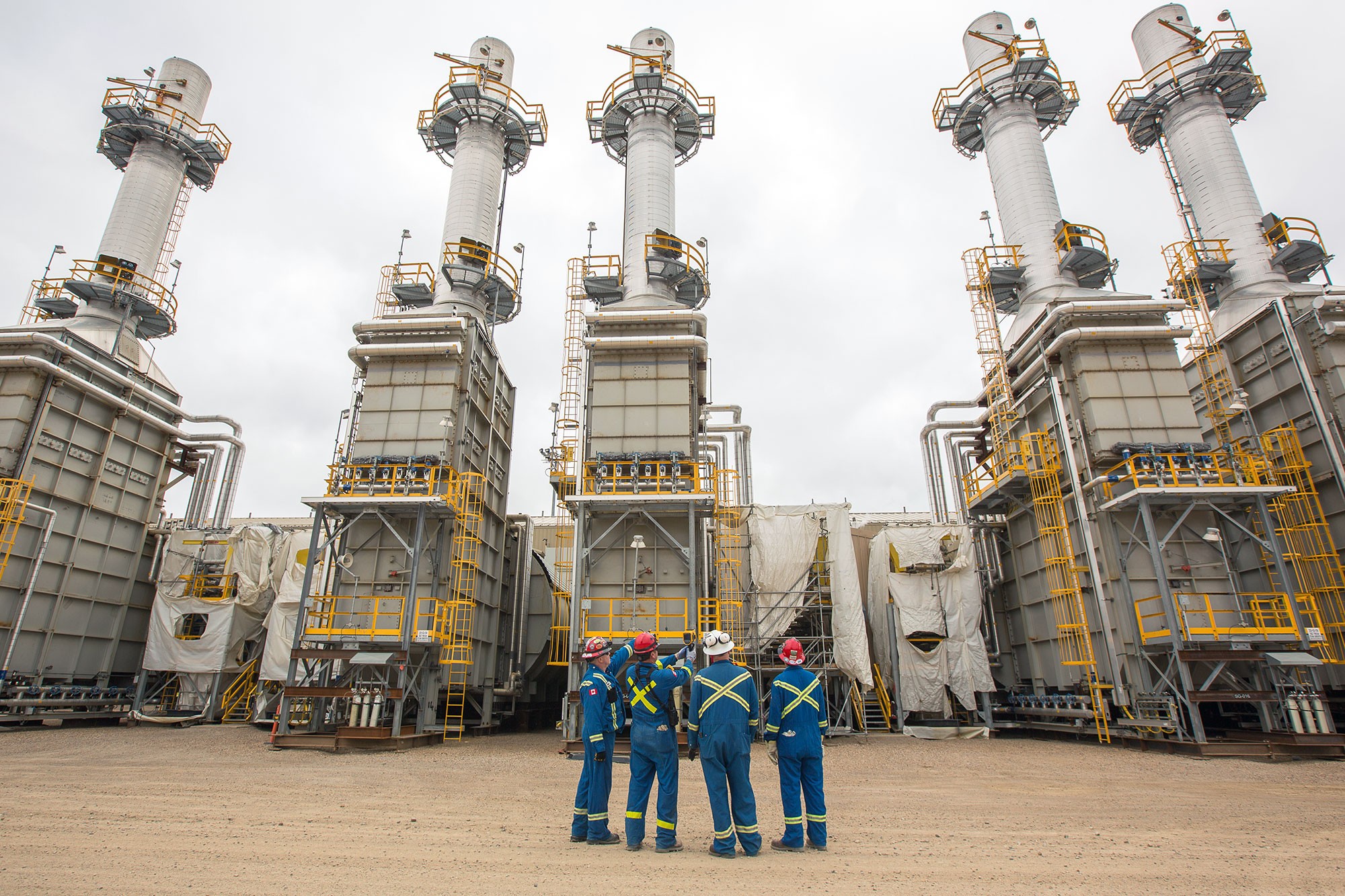 4 workers wearing protective clothing with towers in background